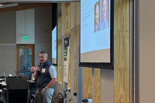 person standing behind podium with large screen on wall behind